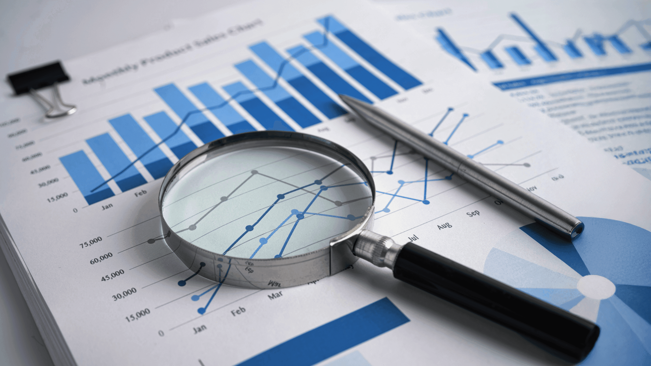 Magnifying glass and pen on financial charts and graphs.