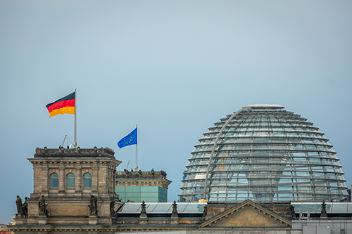 Photo of the Reichstag building in Berlin with German and European Union flags and its glass dome, symbolizing government and legislative environment relevant to aerospace consulting context