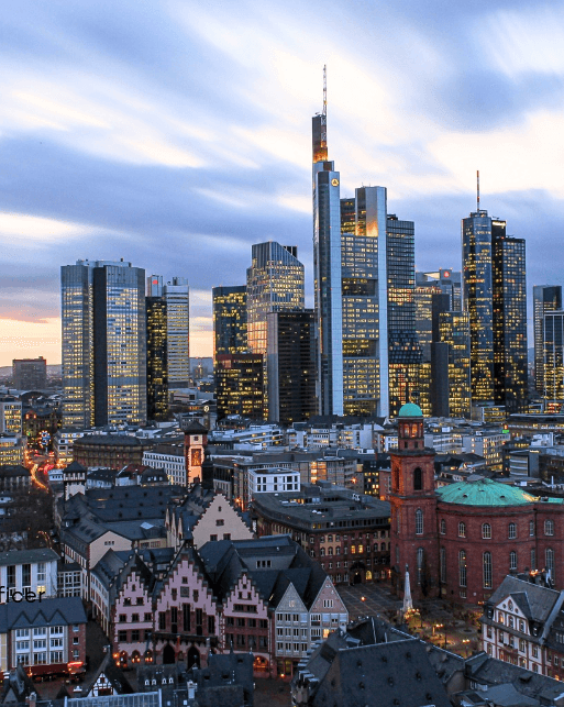 Skyline of Frankfurt with modern skyscrapers and historic buildings in the foreground during dusk.
