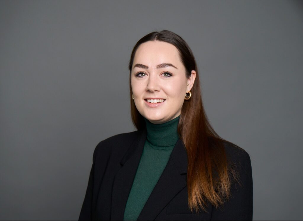 Professional female consultant with long brown hair wearing green turtleneck and black blazer portrait