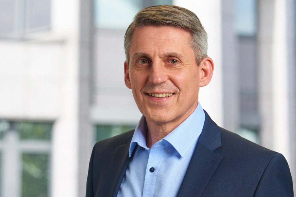 Portrait of Klaus Heininger, a senior consultant with short gray hair wearing a navy suit jacket and light blue shirt, representing H&Z's leadership and expertise in management consulting.