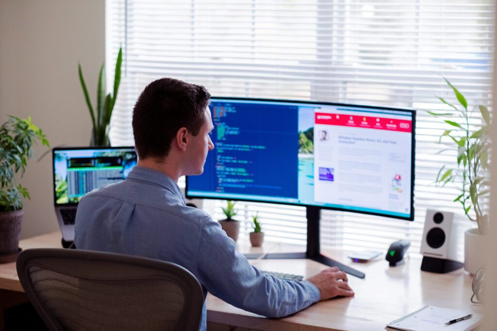 Man working at a desk with dual computer monitors displaying analytics and code, representing H&Z consulting's data-driven approach to IT spending optimization.