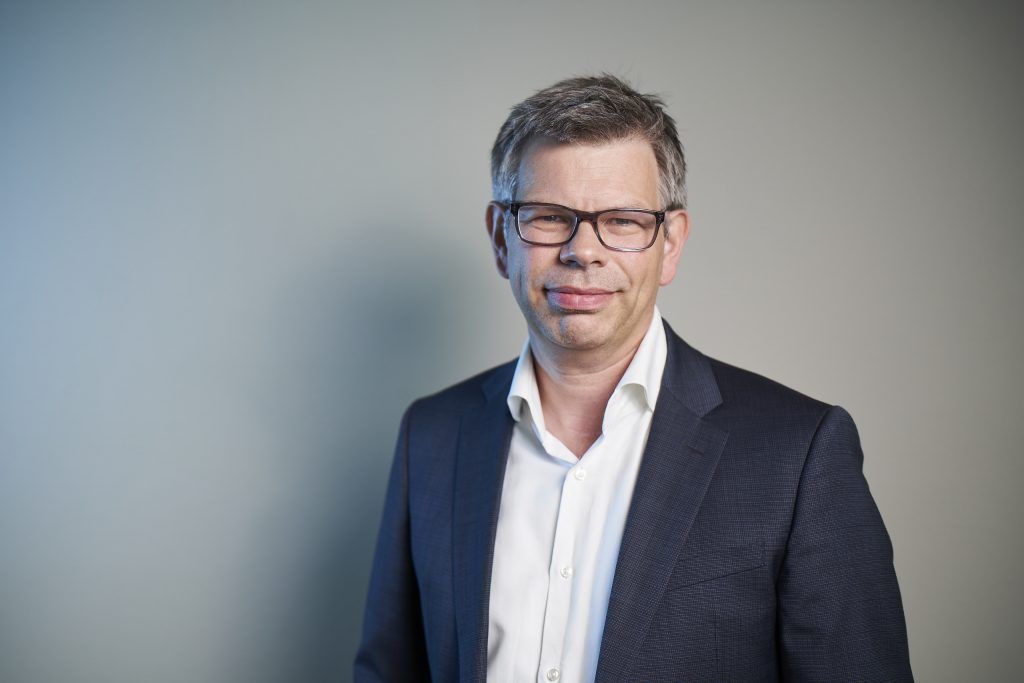 Portrait of Dr. Markus Contzen, senior advisor at H&Z consulting, wearing glasses and a dark suit jacket, standing against a neutral background.