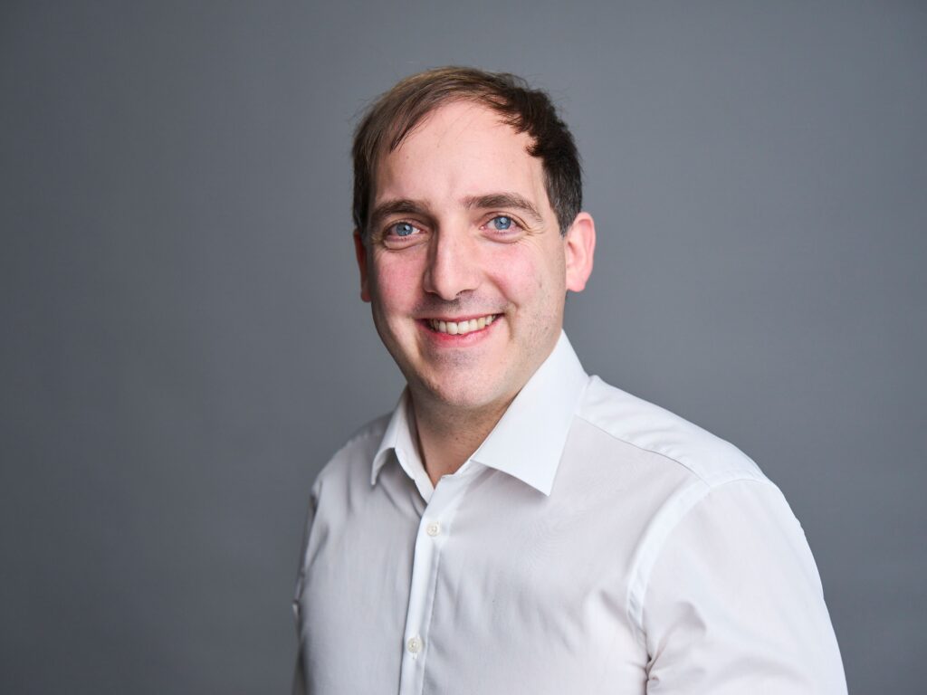 Portrait of a smiling male consultant in a white shirt, conveying approachable professionalism and client-focused consulting expertise.