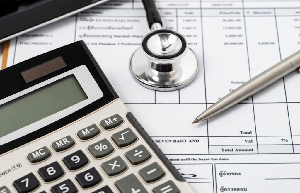 Medical stethoscope, calculator and pen on top of financial documents, representing healthcare cost analysis and optimization in consulting services.