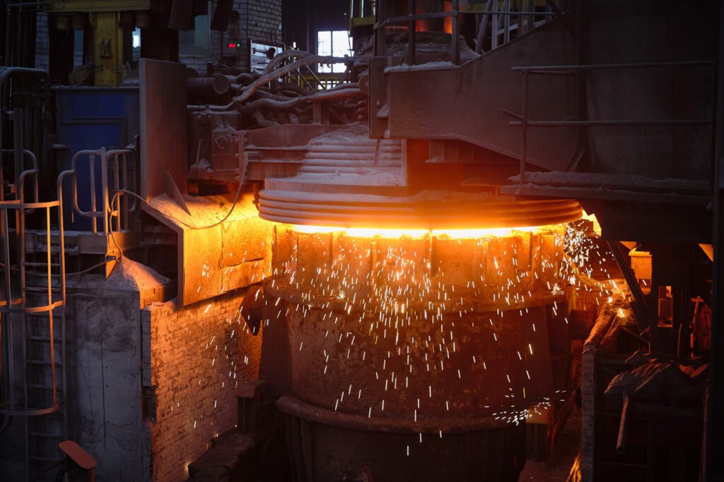 Industrial steel mill scene showing molten metal pouring from a furnace with glowing orange light and sparks, representing heavy industry and manufacturing expertise for consulting projects.