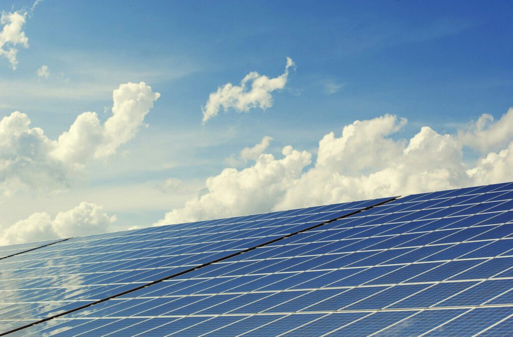 Array of solar panels reflecting a bright blue sky with scattered clouds, illustrating renewable energy and sustainability initiatives relevant to consulting and corporate strategy.