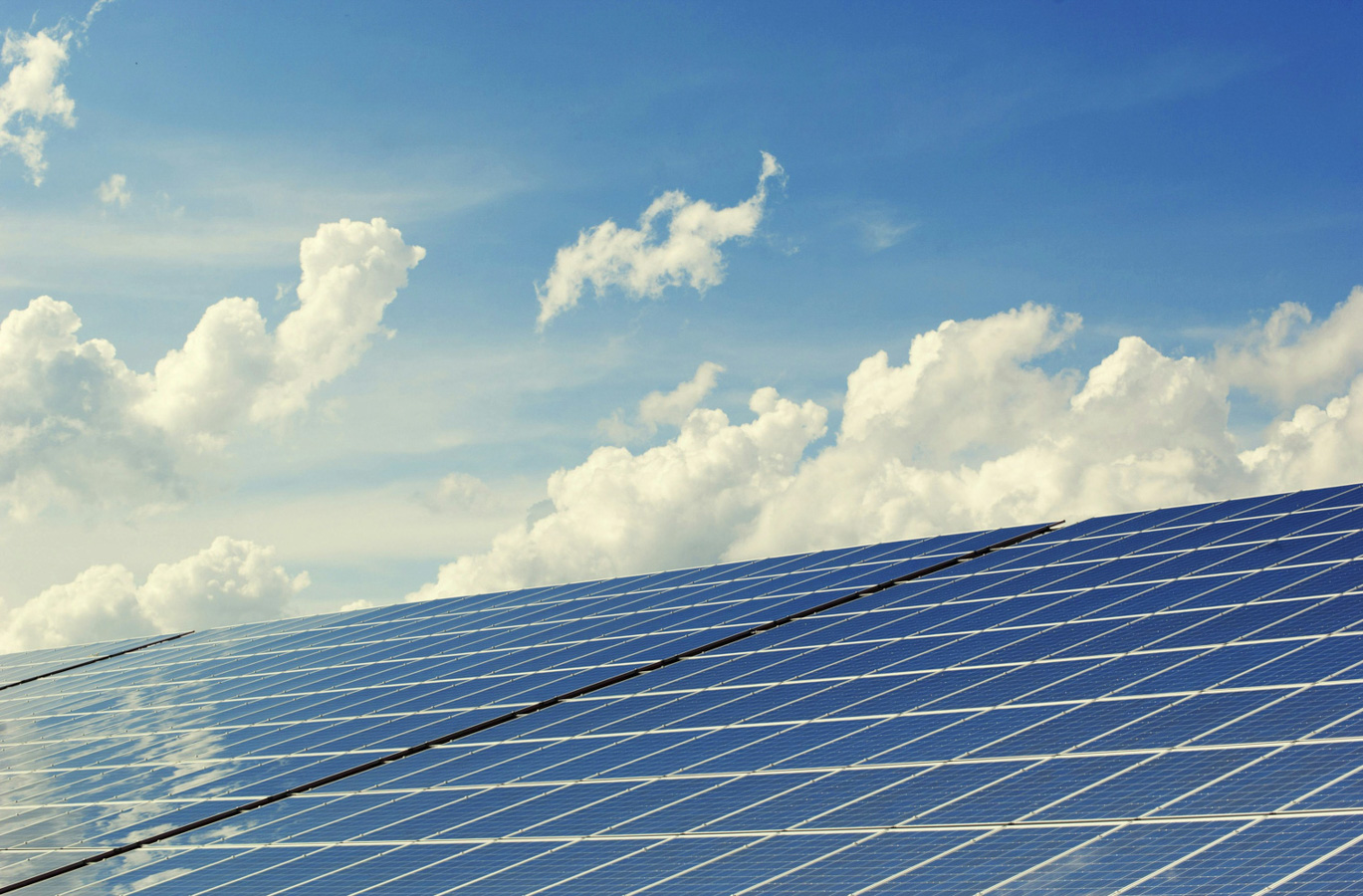 Array of solar panels reflecting a bright blue sky with scattered clouds, illustrating renewable energy and sustainability initiatives relevant to consulting and corporate strategy.
