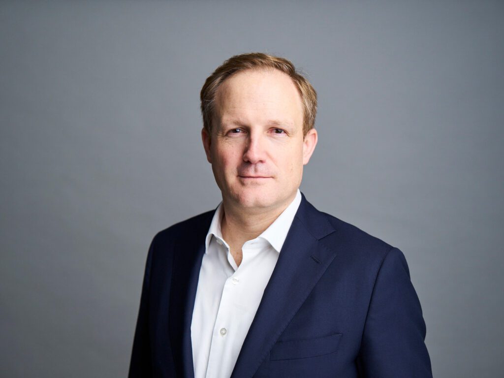 Portrait of Stephan Deussen, a middle-aged male consultant with short blond hair wearing a navy suit and white shirt against a neutral grey background, conveying professionalism and approachable business expertise.