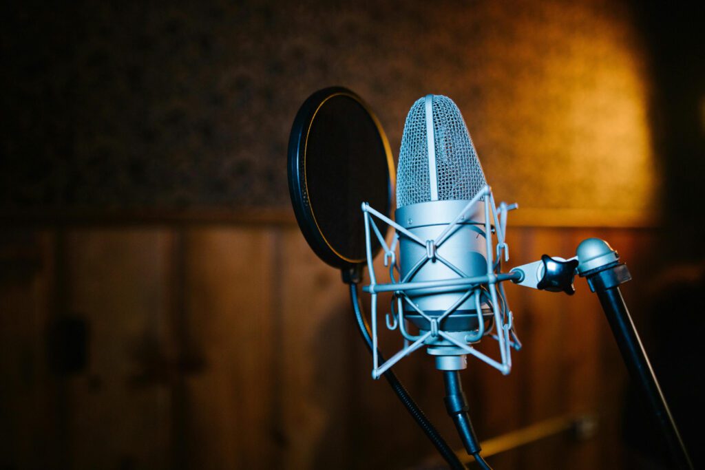 Close-up of a professional studio microphone with pop filter against a blurred studio background, symbolizing high-quality podcast audio production and thought leadership discussions in the consulting sector.