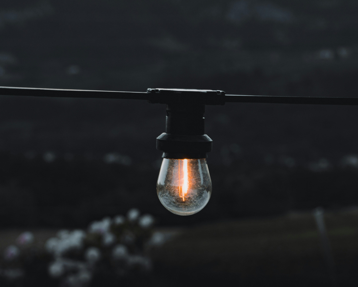 Close-up of a glowing hanging lightbulb on a black cable against a dark background, symbolizing innovative ideas and illumination of strategic insights in consulting services.