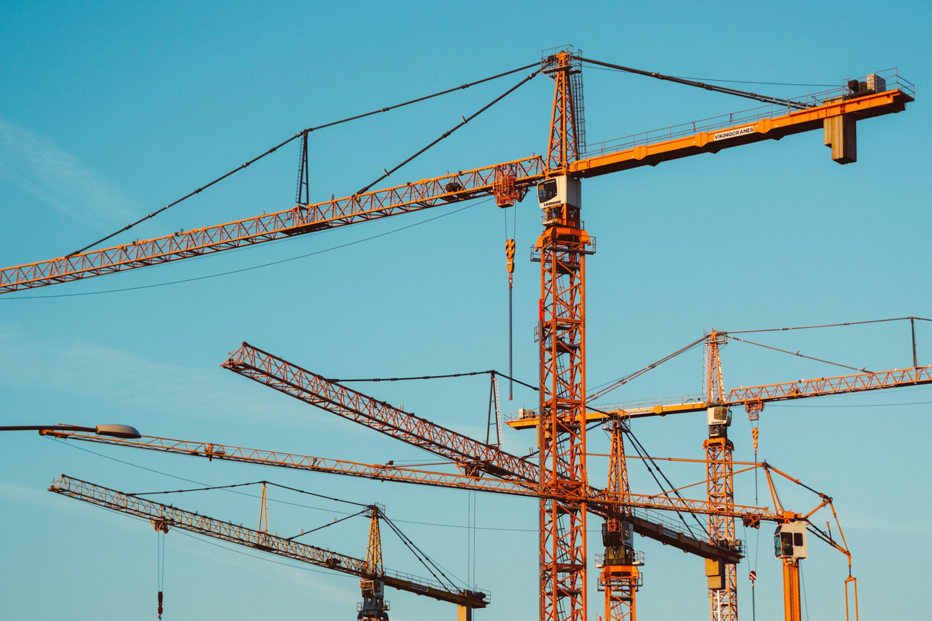 Construction cranes against a clear blue sky, symbolizing growth and development – HZ Group consulting infrastructure projects