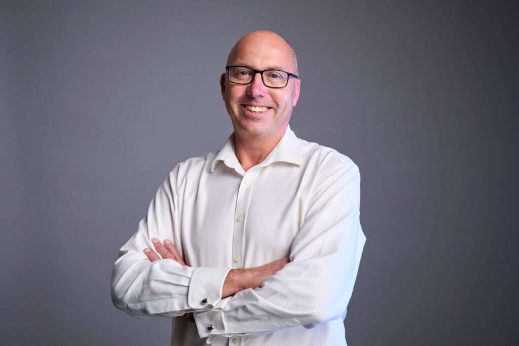 Portrait of bald male consultant wearing glasses and a white shirt, standing with arms crossed, representing confidence, integrity and consulting expertise.