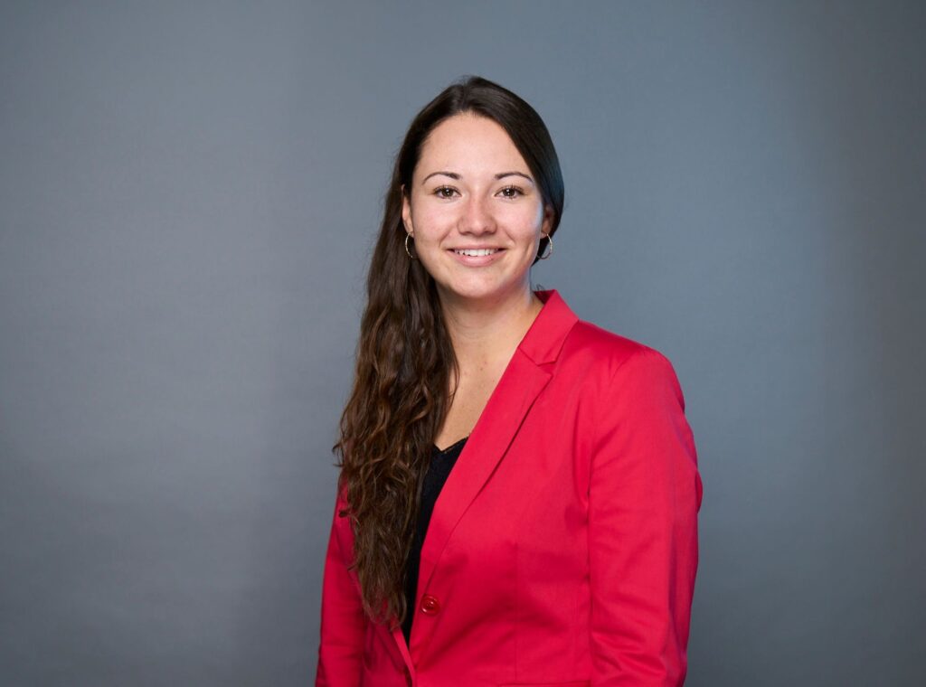 Professional headshot of consultant Sarah Vatter wearing a red blazer and black top, smiling against a gray background