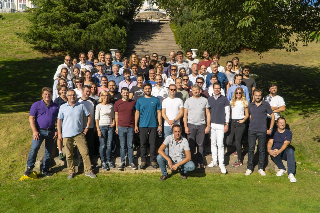 Large group of consultants gathered outdoors on a sunny hillside for a team photo during a company retreat, symbolizing camaraderie and team spirit in consulting projects