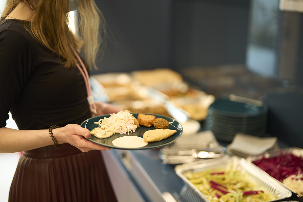 Person holding a plate of food at a buffet table during an H&Z consulting company event, illustrating hospitality and networking over business meals.