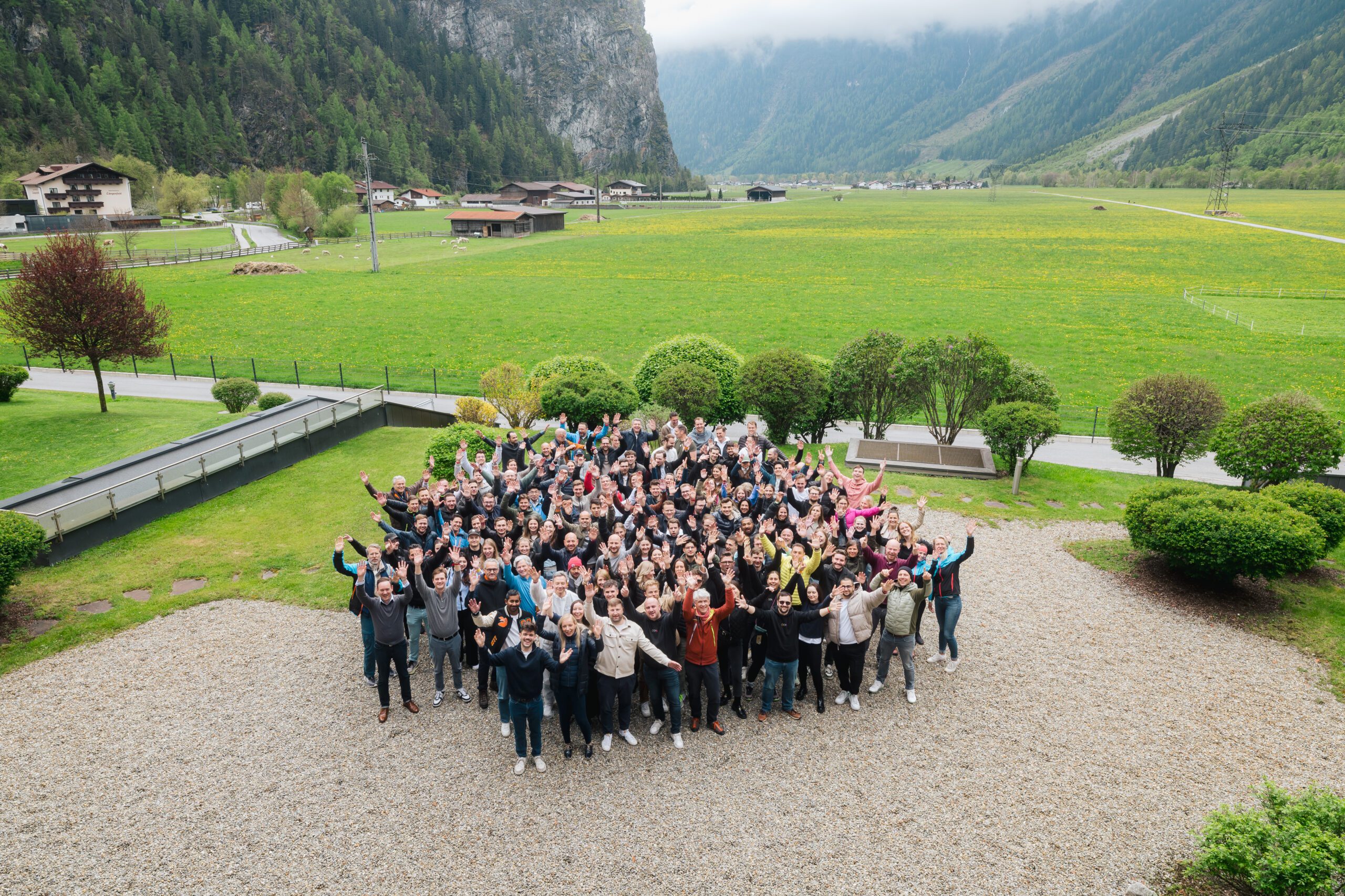 Large group of H&Z consulting colleagues at an outdoor team event in a scenic mountain valley, gathered together with raised hands to celebrate collaboration.