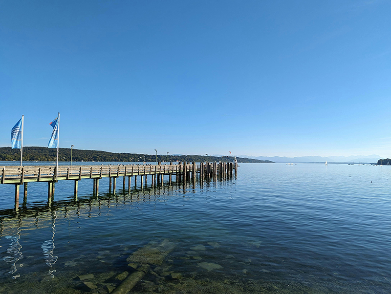 Pier extending into a tranquil lake with flags and clear water at Haselhors, representing serene environment inspiring business consulting and strategic thinking.