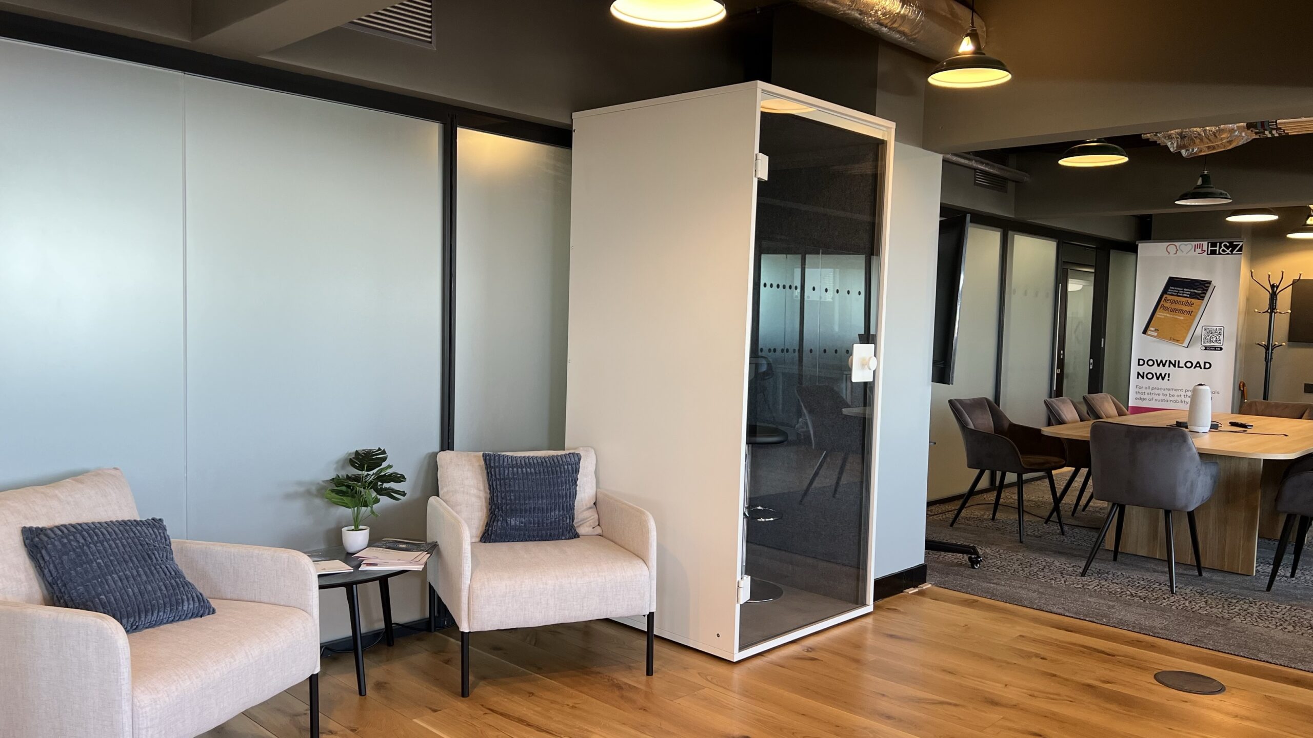 Modern consulting office interior with armchairs, small acoustic phone booth and meeting table on wooden floor