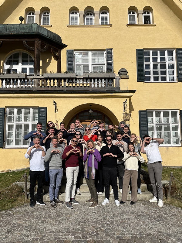 H&Z consulting team group photo in front of a historic yellow villa, colleagues making heart gestures and smiling during a company retreat, symbolizing teamwork and corporate culture.