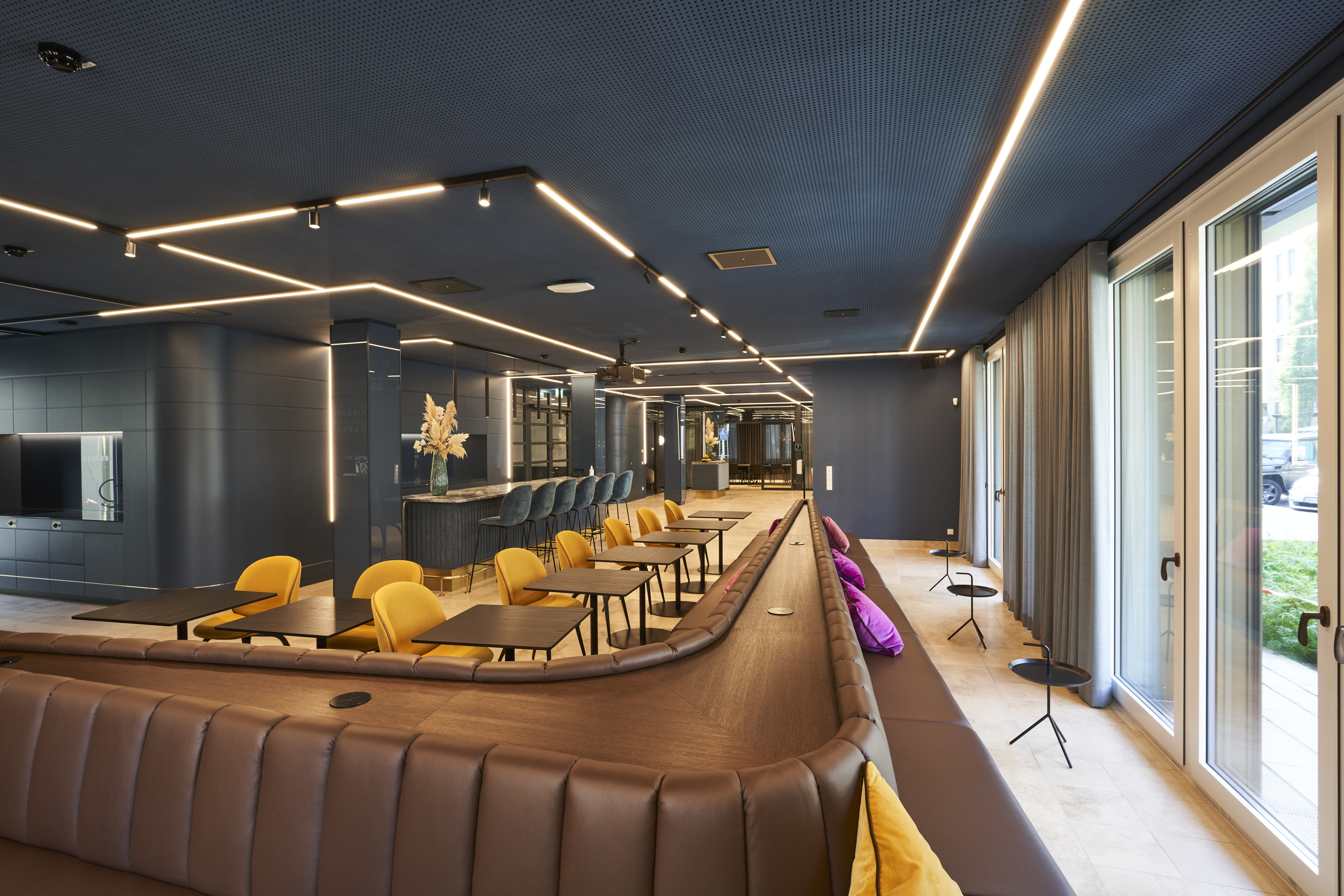 Contemporary office lounge area with long leather bench, yellow chairs and sleek lighting, designed for client meetings and corporate events at a consulting firm