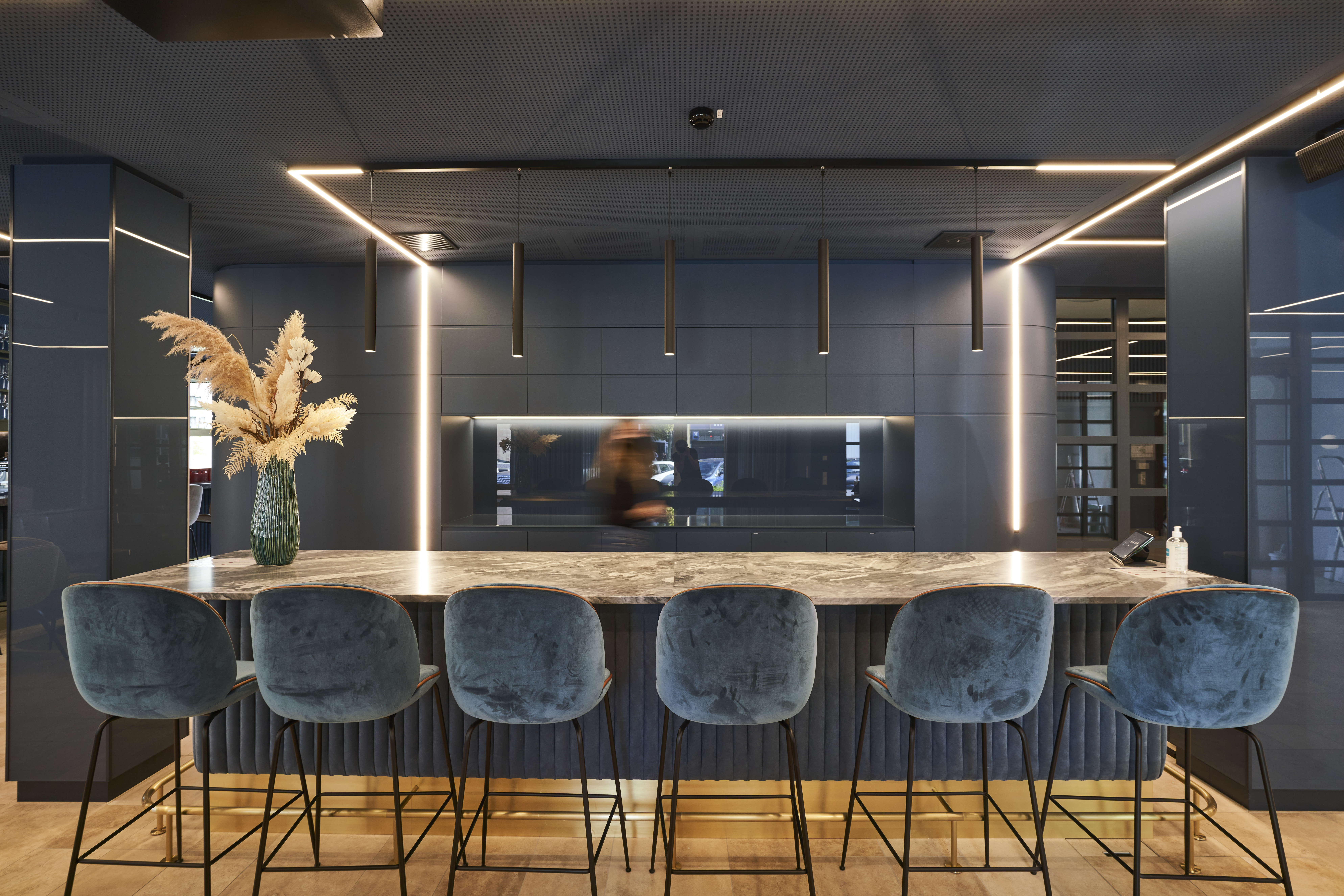 Modern corporate lounge bar with marble counter and velvet blue stools for informal client meetings and networking at a consulting firm