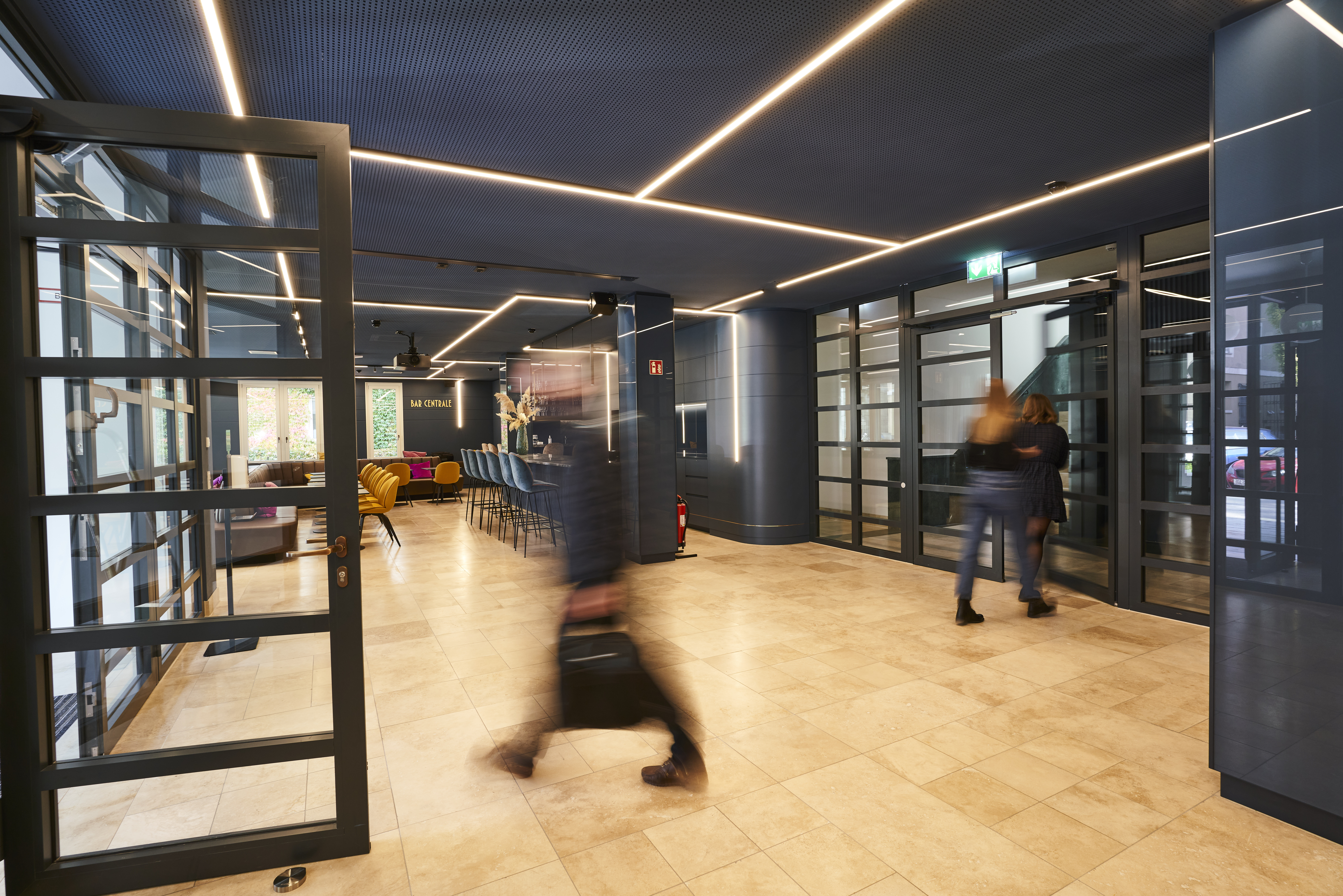 Blurred office professionals walking through modern consulting office corridor with glass doors and contemporary ceiling lights