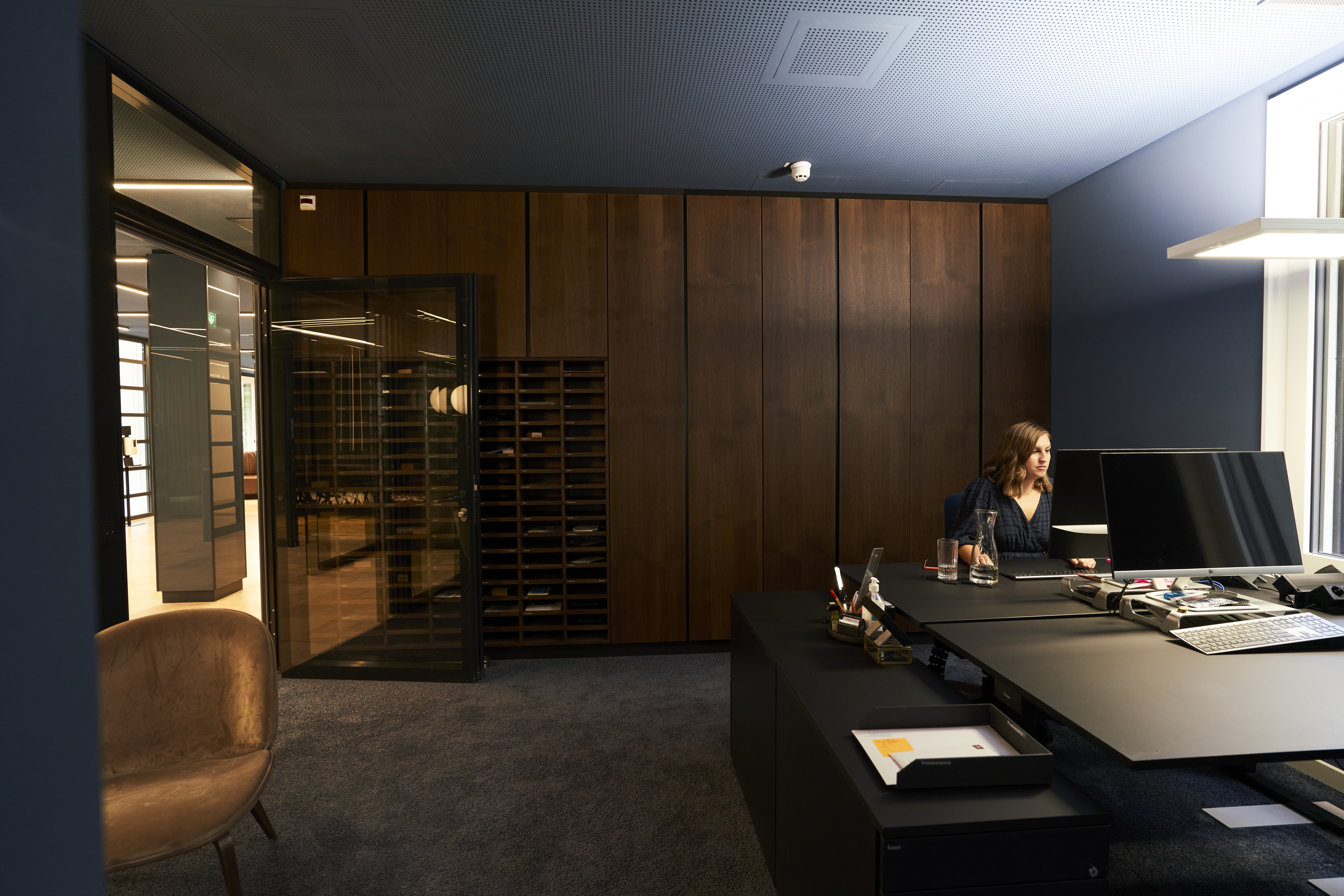 Luxurious executive office with wooden wall panels, spacious desk with multiple monitors and a consultant working, illustrating high-level management consulting environment