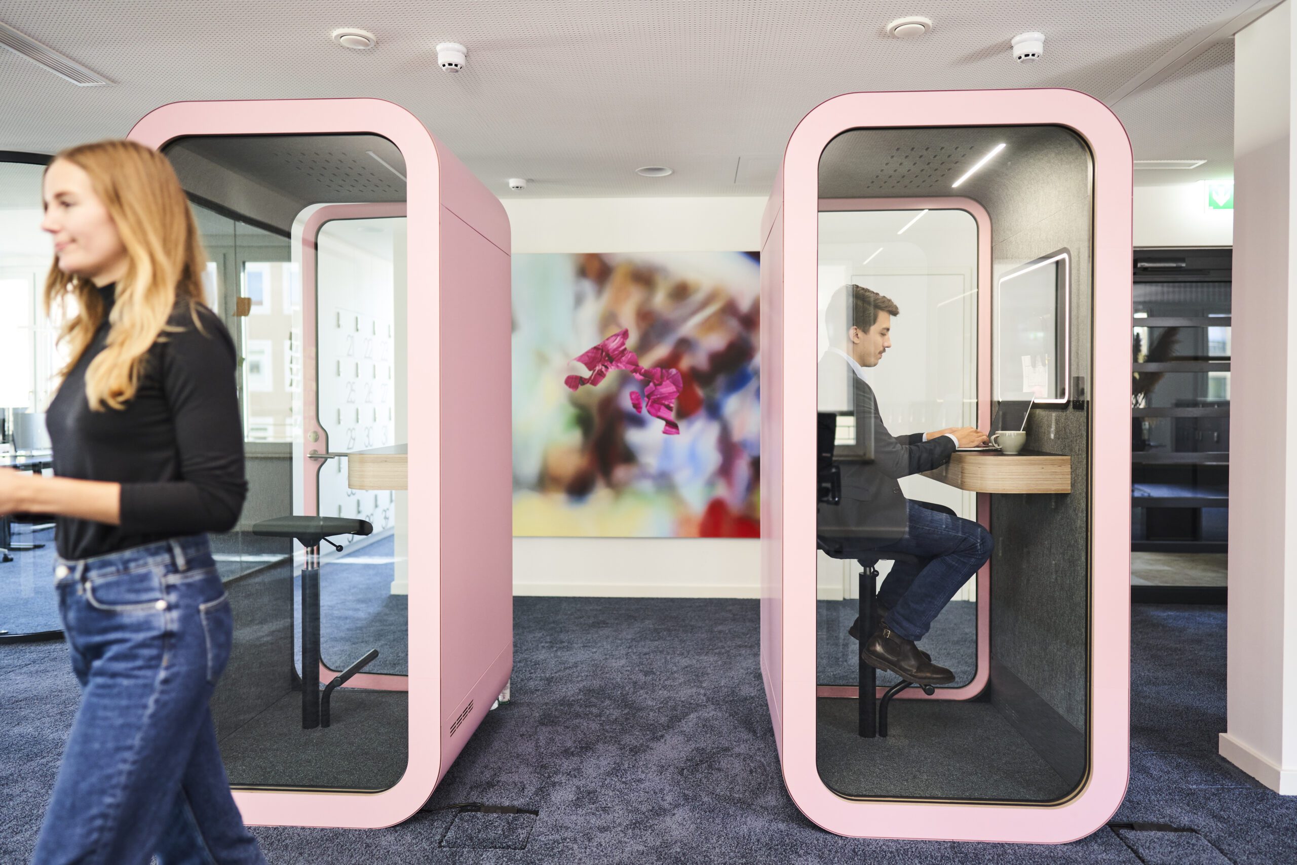 Consulting professionals utilizing modern pink phone booths in an open office environment reflecting creative communication and innovation