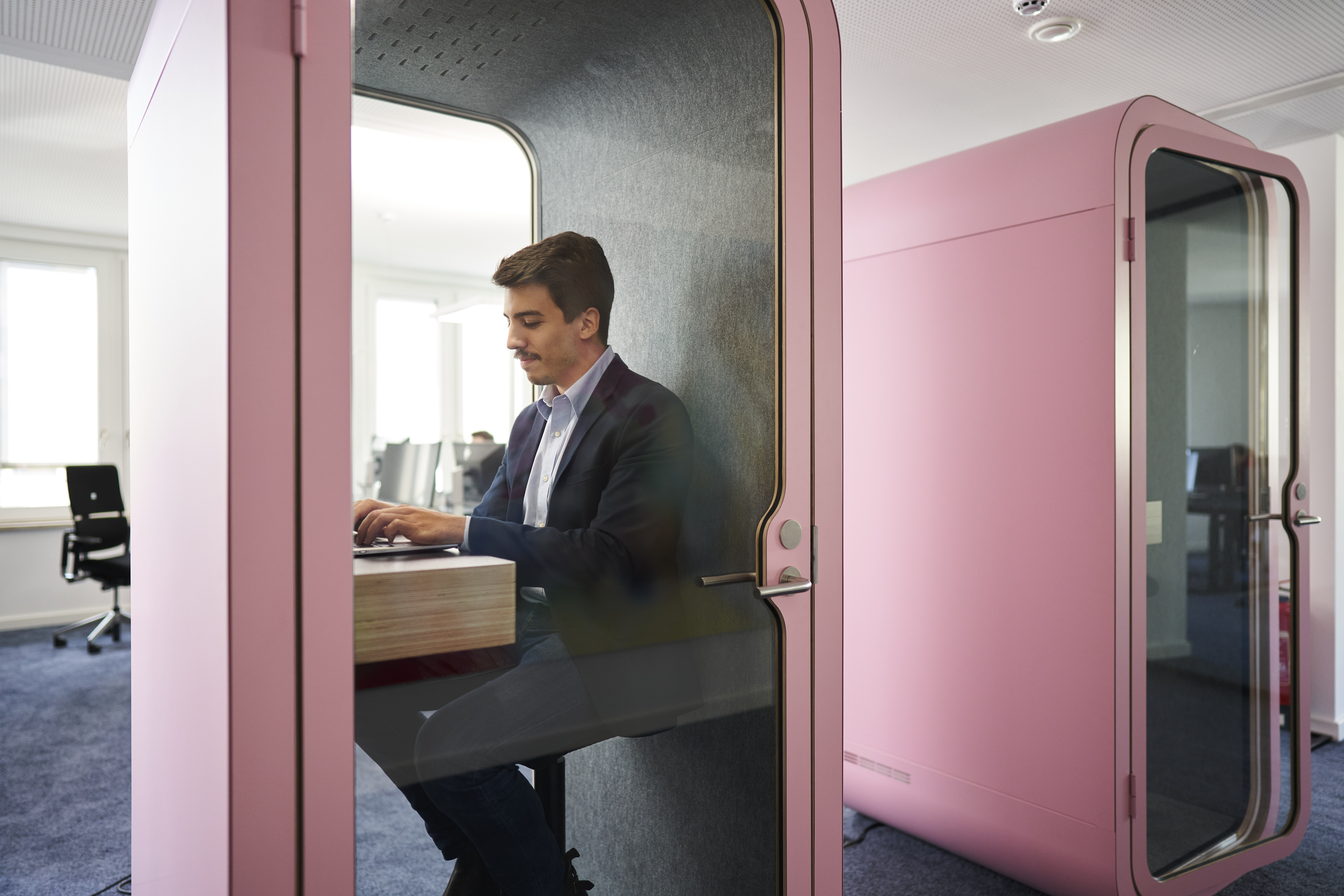 Male consultant working on laptop inside pink private booth in a modern open office environment demonstrating focus and productivity
