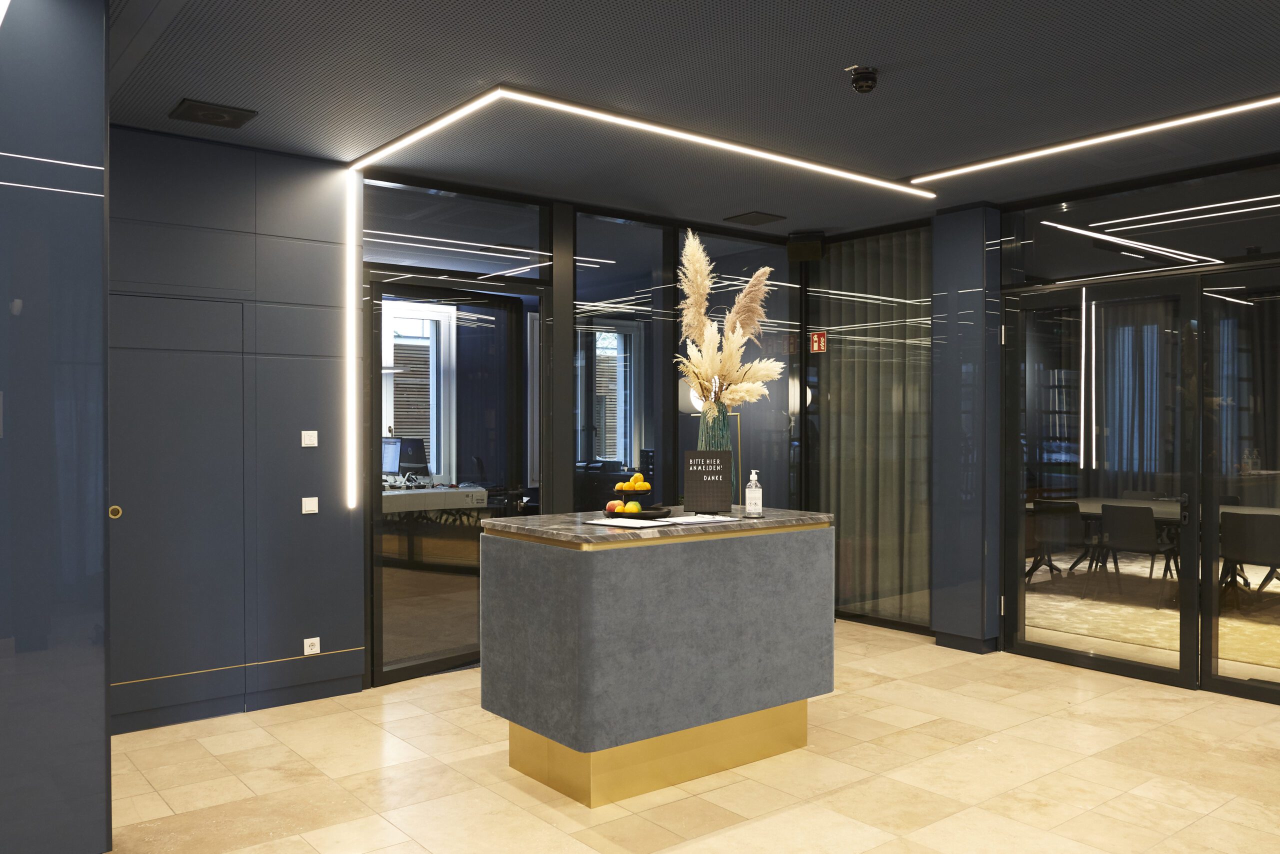 Elegant office lobby with modern island counter decorated with vase and fruit, surrounded by dark walls and glass partitions, representing professional reception area for consulting clients