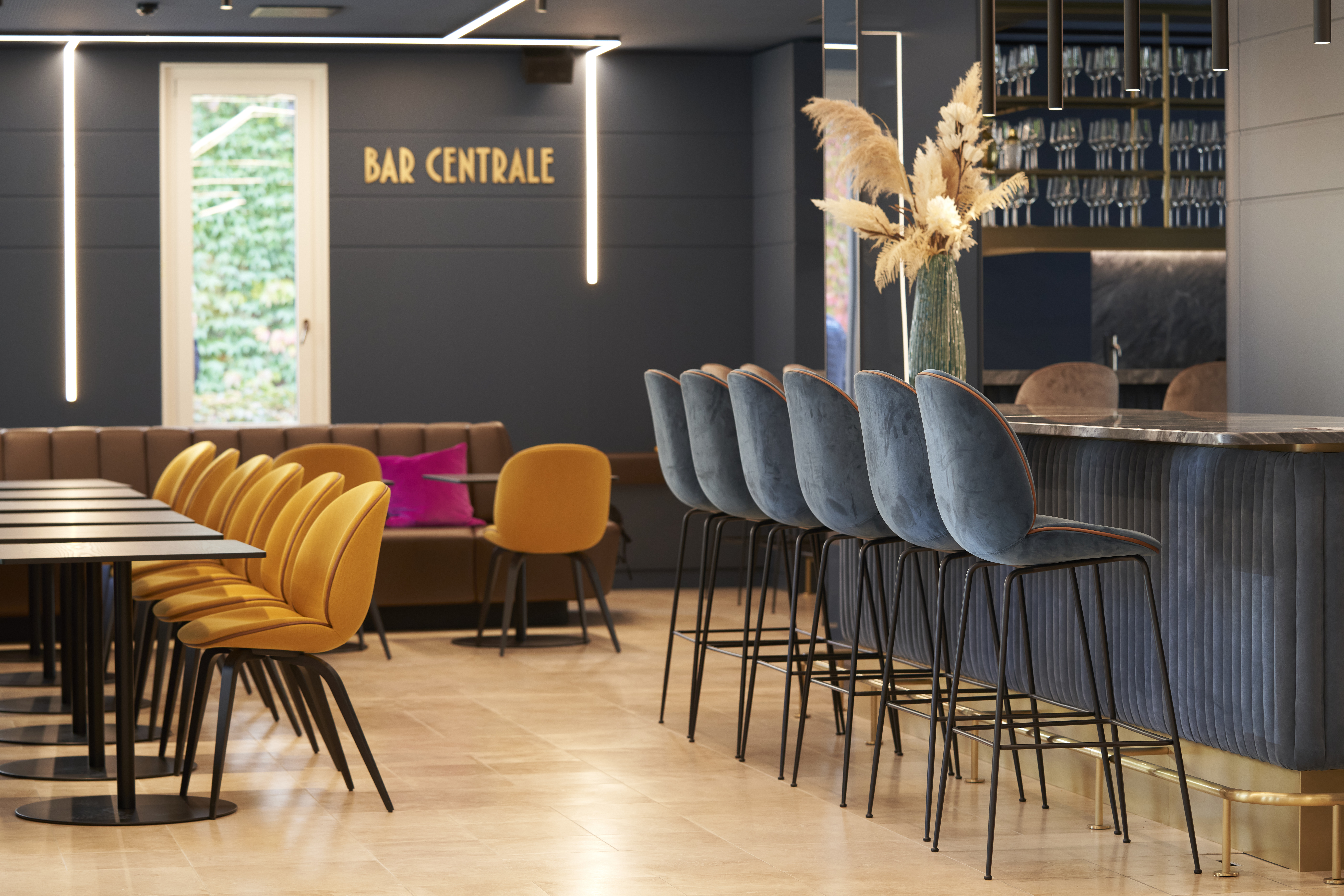 Stylish Bar Centrale lounge area with golden chairs, velvet blue bar stools, and modern bar counter for informal meetings and networking at a consulting firm
