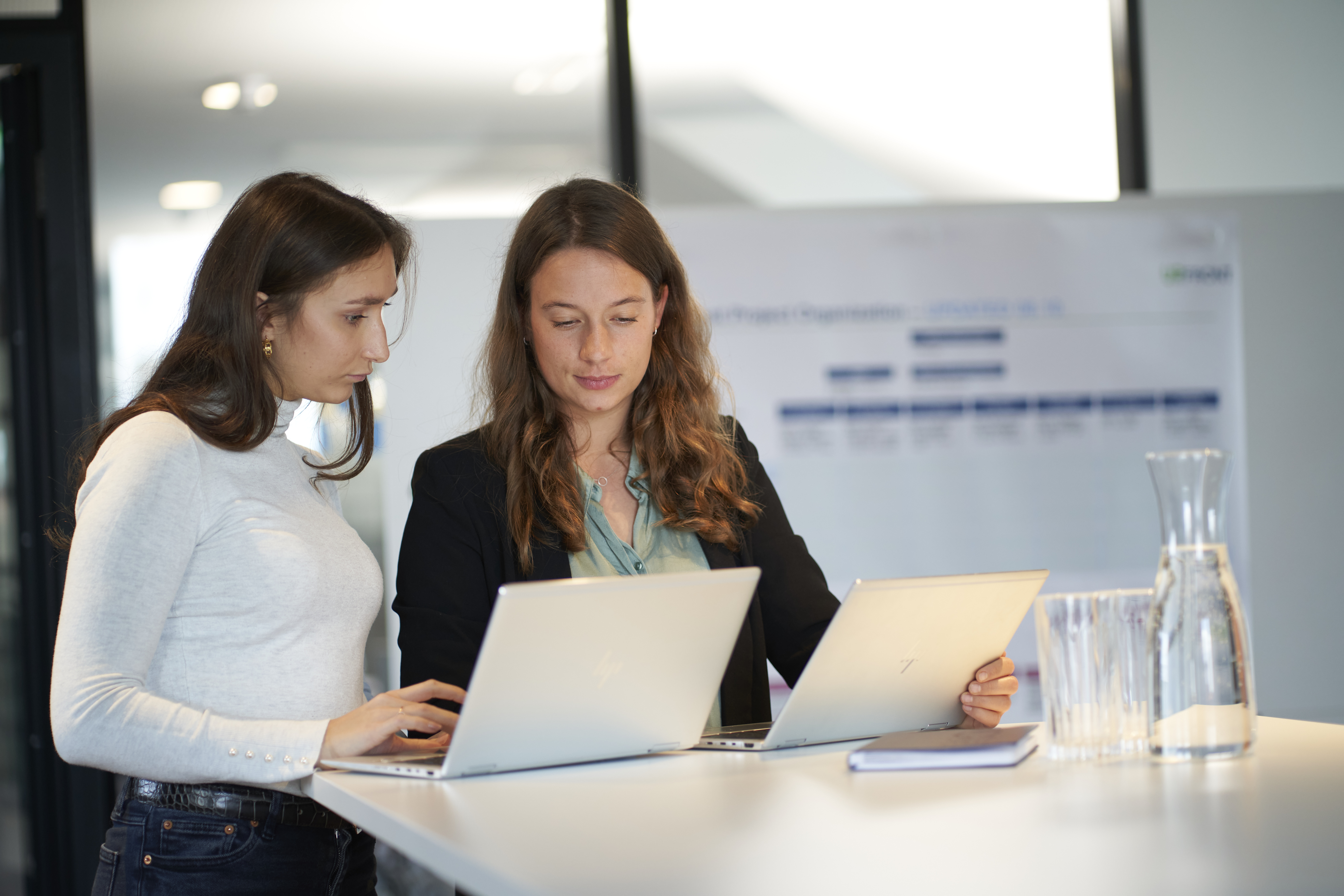 Two female consultants discussing work over a laptop at office table with charts in background