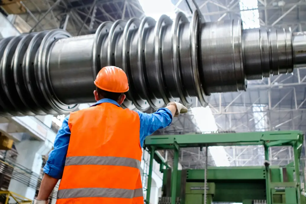 Worker in orange safety vest inspecting large industrial machinery as part of technical facility management cost reduction consulting project
