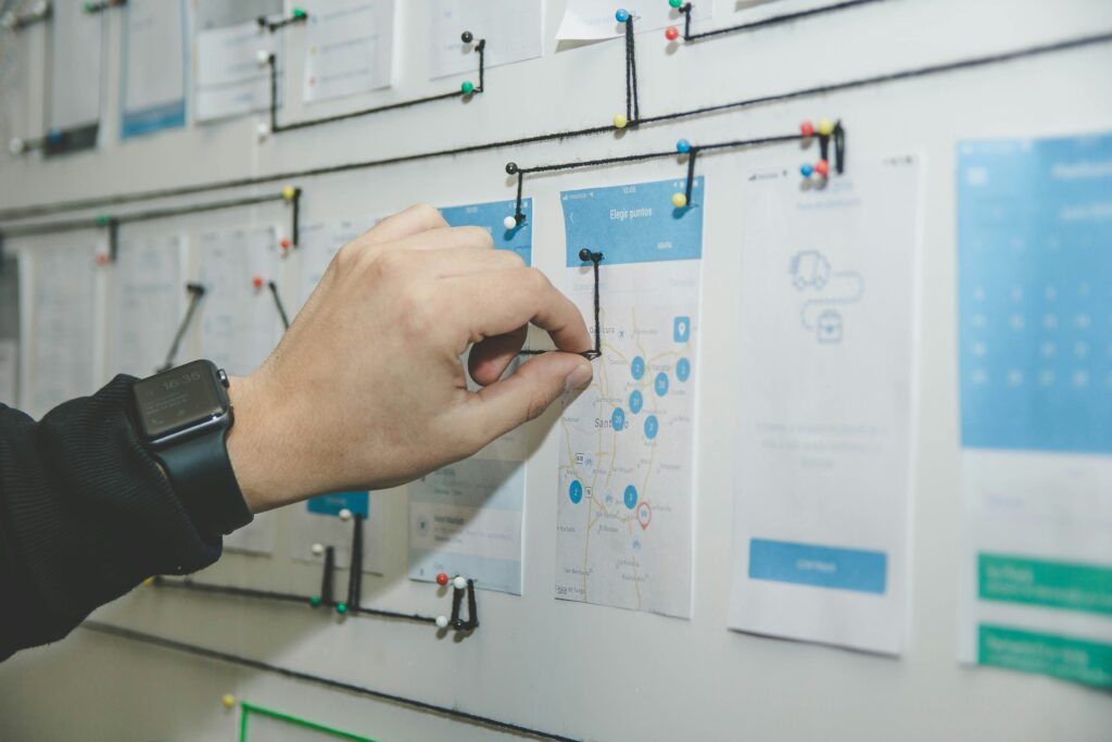 Close-up of a consultant's hand wearing a smartwatch pinning notes and diagrams onto a planning board, symbolizing strategic project planning and agile workflow in consulting
