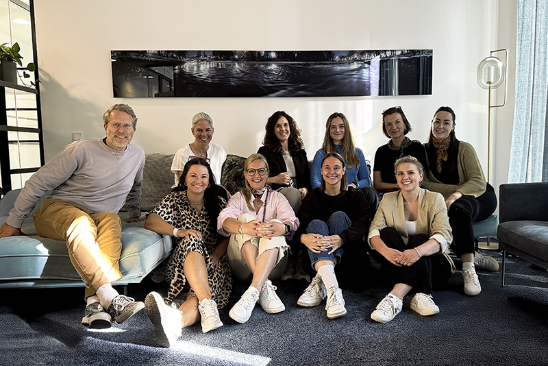 Consulting firm HR team group photo of professionals sitting together in a modern office, symbolizing collaborative business strategy culture.