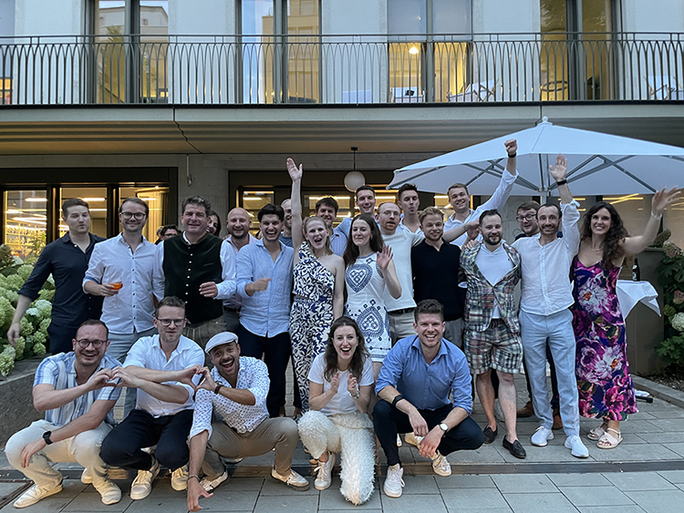 H&Z consulting team celebrating together at an outdoor evening event, group of colleagues raising hands and smiling at a company gathering.