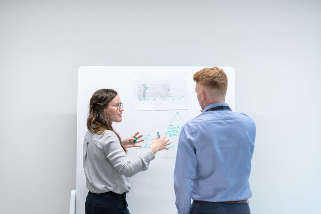 Two consultants collaborating at a whiteboard, brainstorming and sketching diagrams during a strategic planning workshop, representing collaborative consulting sessions.