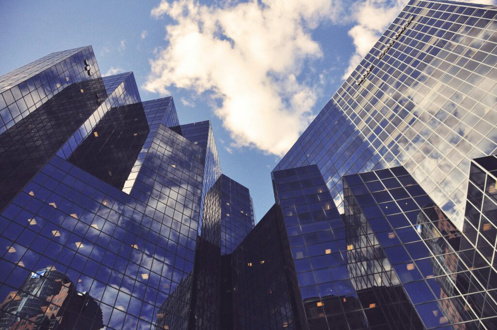 Cluster of modern glass skyscrapers reflecting the sky and clouds, representing corporate headquarters, urban growth and strategic consulting for real estate and technology firms