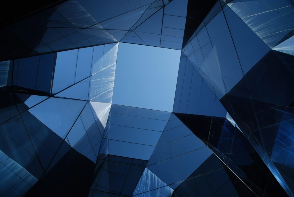 Abstract view looking up through glass building facades reflecting the blue sky, symbolizing transparency, modern architecture, and visionary perspectives in consulting.