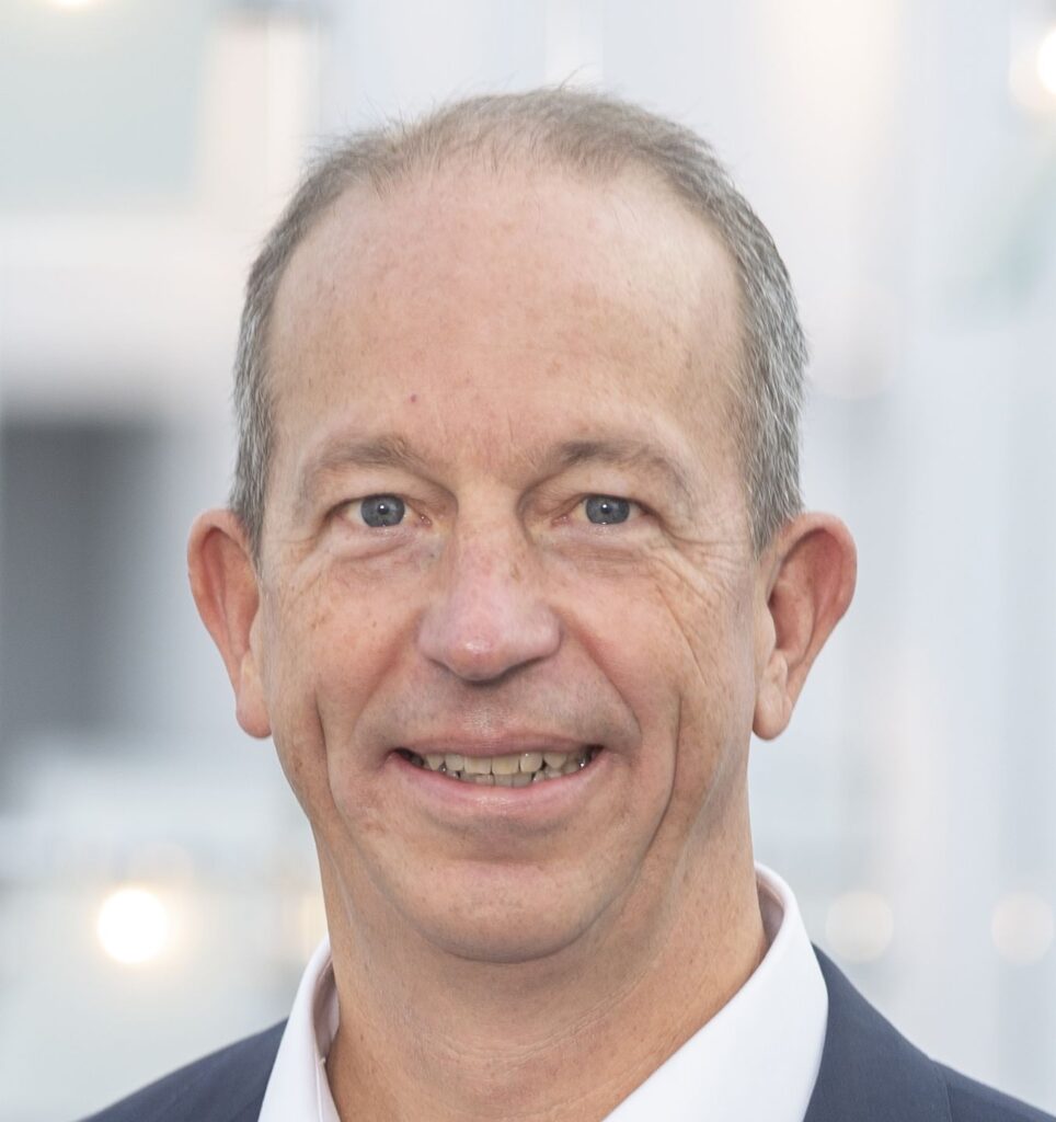 Headshot of a smiling male business professional in a suit, representing consulting leadership
