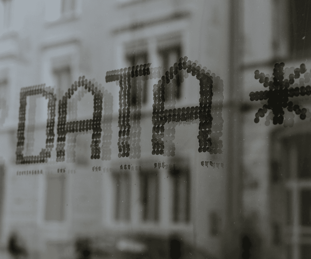 Word "DATA" formed by black dots on a glass window with a blurred city background and star symbol, representing data-driven insights and analytics in modern business consulting.