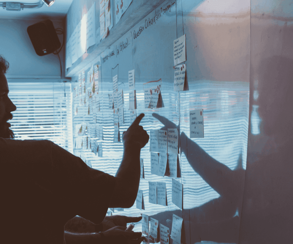 Silhouette of a person pointing at a glass wall covered with sticky notes and diagrams, symbolizing strategic planning and collaborative brainstorming in consulting.