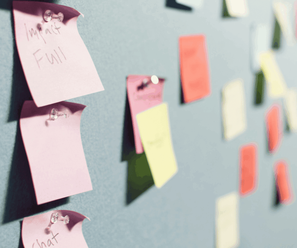 Colorful sticky notes pinned on a board with thumbtacks, representing brainstorming and idea generation during consulting workshops.