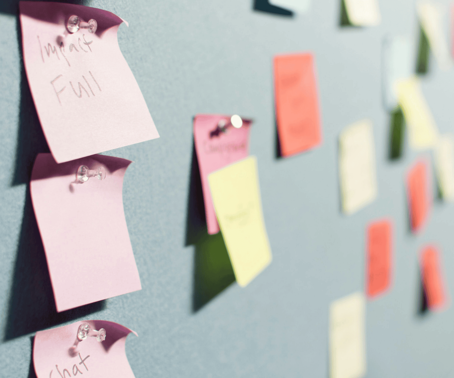 Colorful sticky notes pinned on a board with thumbtacks, representing brainstorming and idea generation during consulting workshops.