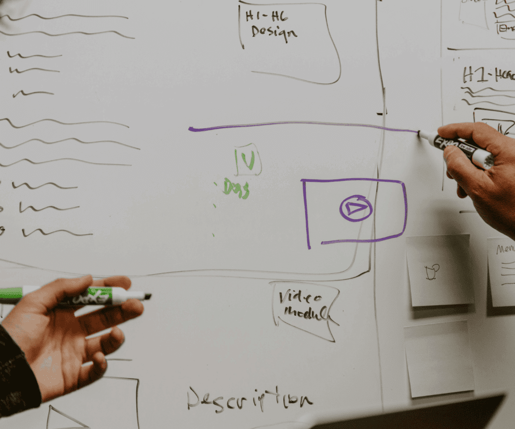 Collaborative brainstorming session with hands sketching diagrams on a whiteboard, illustrating strategic planning and creative problem-solving in our consulting projects.