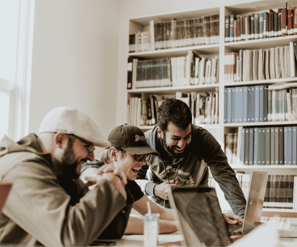 Group of colleagues laughing together while collaborating on a laptop in a relaxed office environment, representing team spirit and creative brainstorming in consulting.