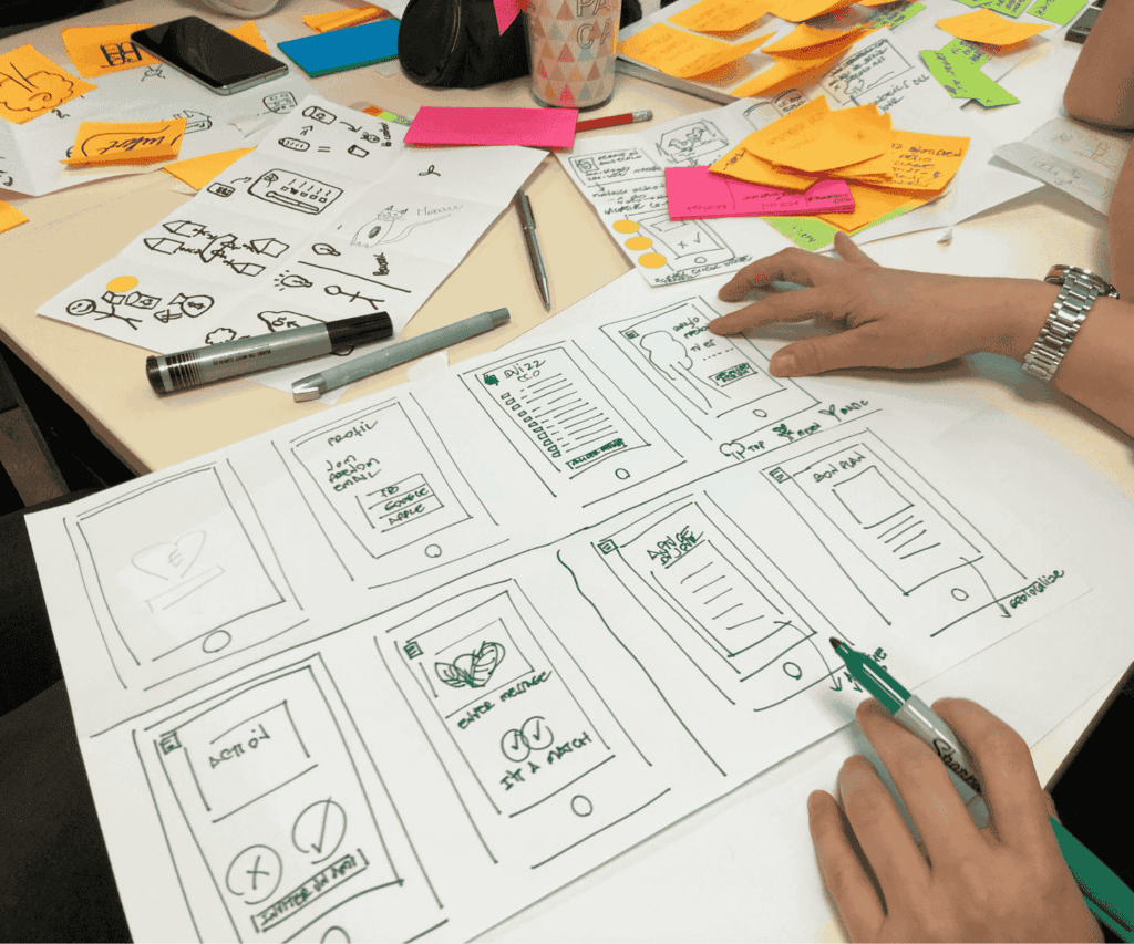 Hand drawing user interface sketches for a mobile app on paper during a design thinking workshop, illustrating creative planning and customer focused consulting services.