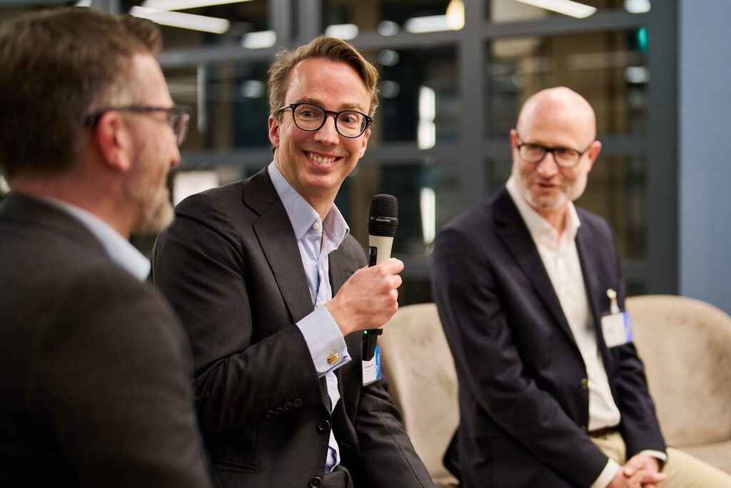 Three speakers smiling during a panel discussion, one holding a microphone | H&Z