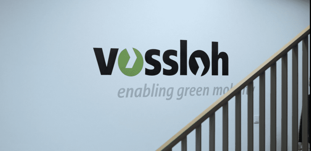 Company signage on a wall with the tagline "enabling green mobility" behind a staircase railing, representing corporate sustainability focus and infrastructure services.